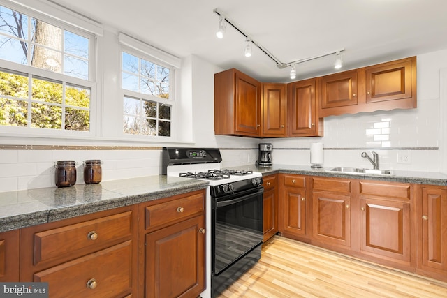 kitchen with a sink, range with gas stovetop, light wood-style flooring, and brown cabinetry