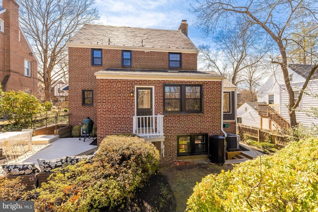 back of property with brick siding, central AC unit, a chimney, and fence