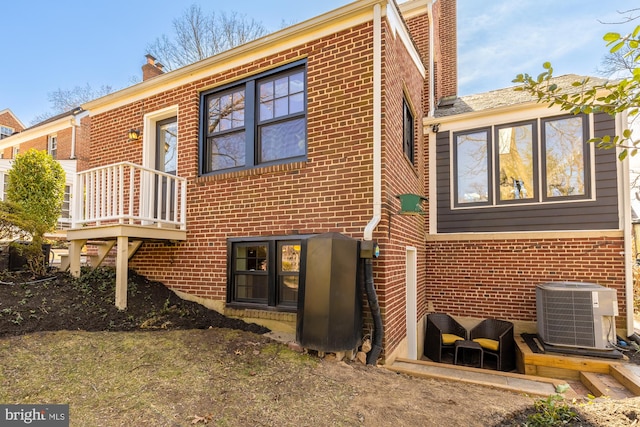 rear view of property featuring brick siding, cooling unit, and a chimney