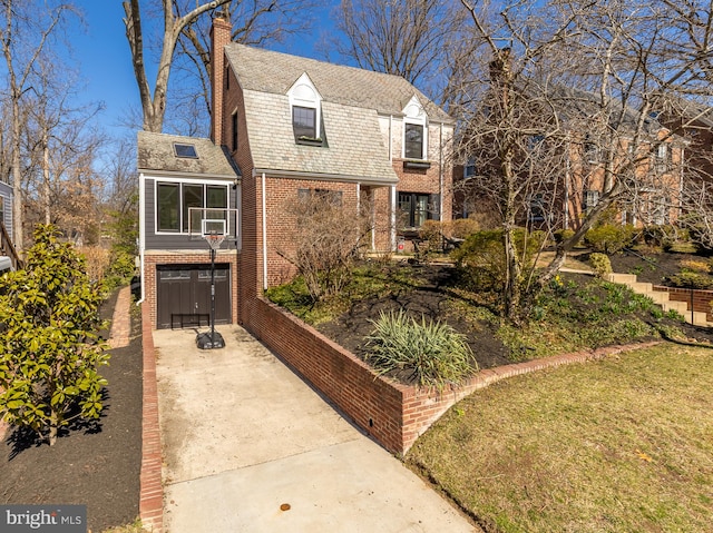 view of front of house featuring brick siding, an attached garage, a gambrel roof, a chimney, and driveway