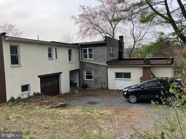 rear view of property with stucco siding, a chimney, and a garage