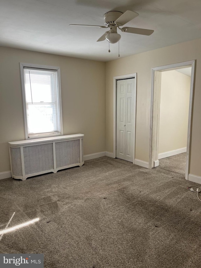 unfurnished bedroom with ceiling fan, radiator, and carpet flooring