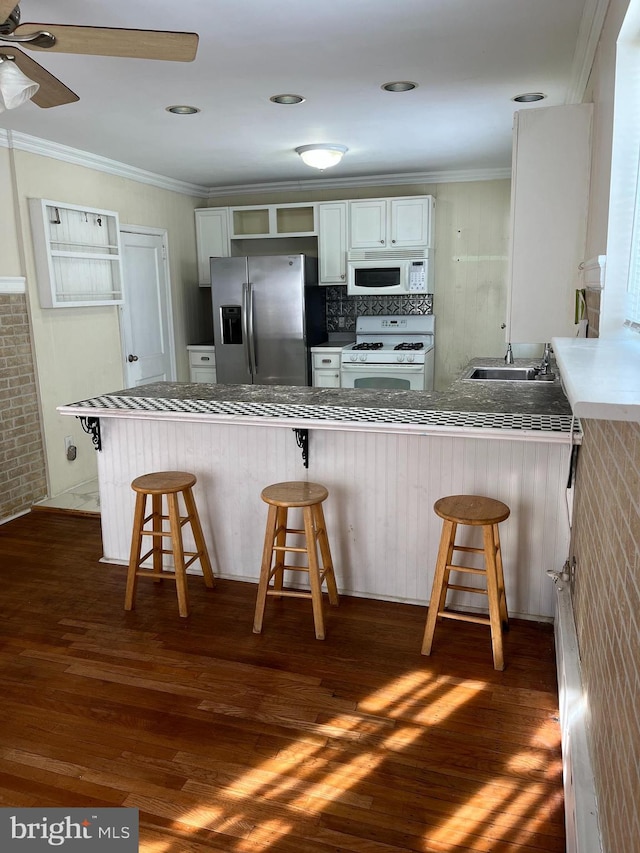 kitchen with white cabinets, kitchen peninsula, white appliances, and a breakfast bar area