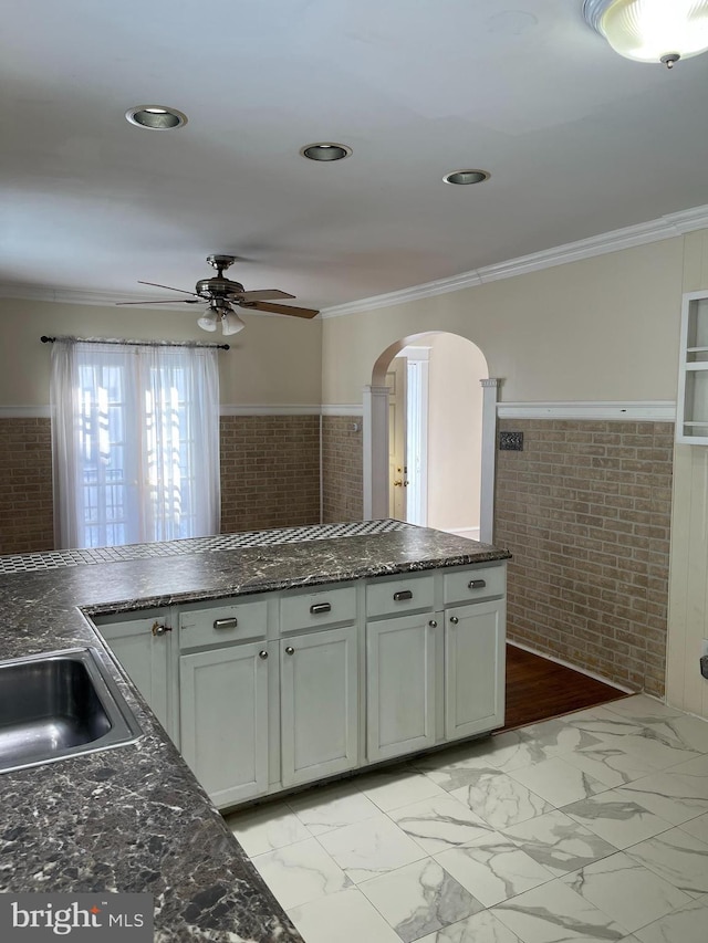 kitchen with ceiling fan, brick wall, crown molding, and white cabinetry