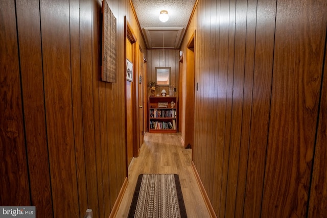 corridor featuring wood walls, a textured ceiling, and light wood-type flooring