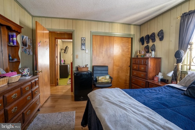 bedroom with light hardwood / wood-style flooring, a textured ceiling, wooden walls, and a closet