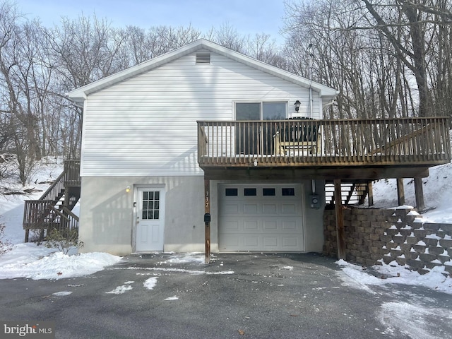 snow covered rear of property with a wooden deck and a garage