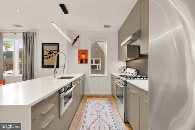 kitchen featuring gray cabinetry, stainless steel appliances, pendant lighting, sink, and backsplash