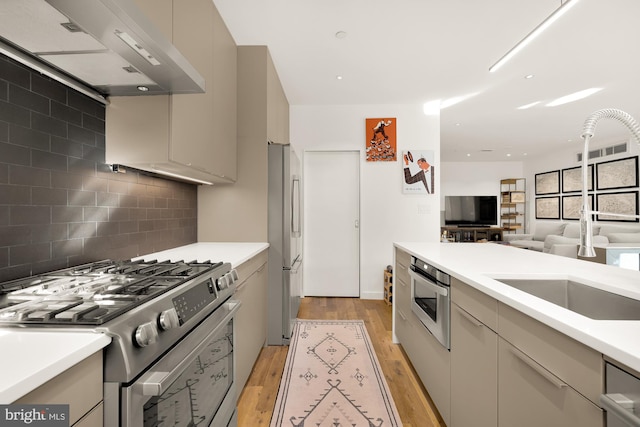 kitchen with sink, wall chimney exhaust hood, light wood-type flooring, backsplash, and appliances with stainless steel finishes