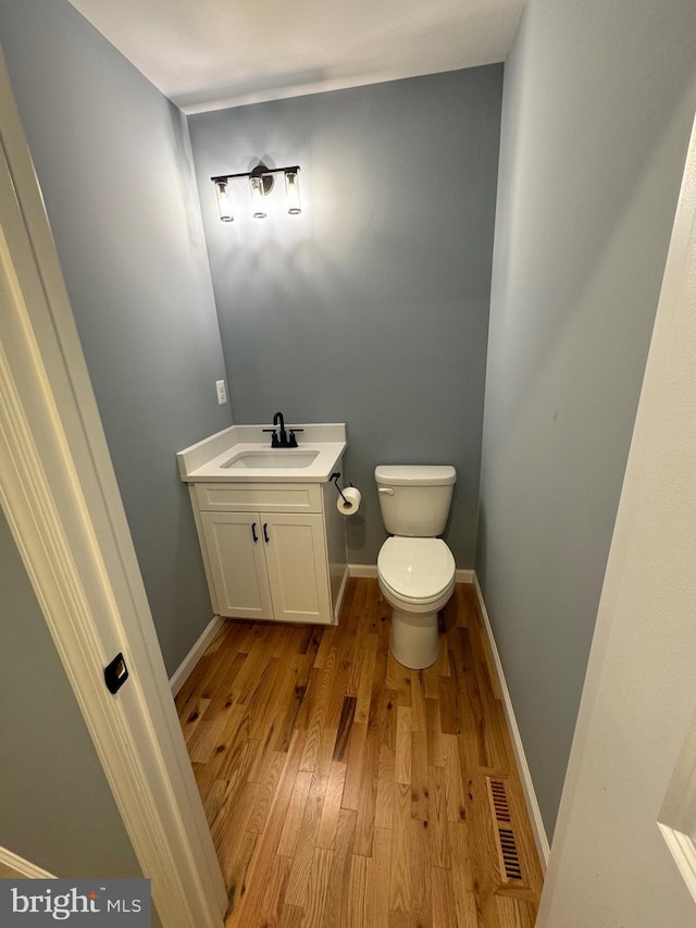 half bathroom with baseboards, visible vents, toilet, and wood finished floors