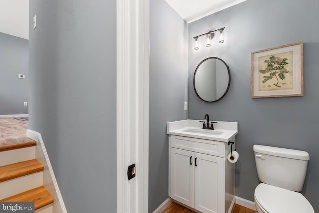 half bath with baseboards, vanity, and toilet