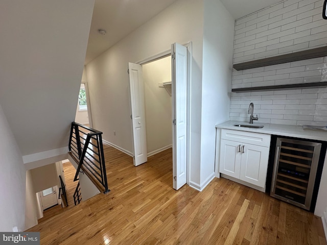 bar featuring white cabinets, light wood-type flooring, sink, and wine cooler