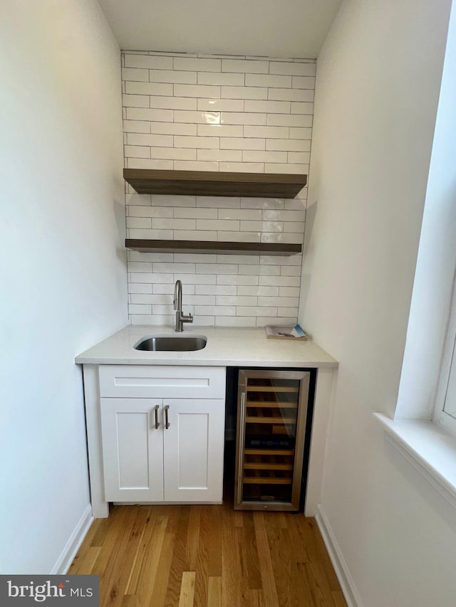 bar with backsplash, white cabinets, sink, wine cooler, and light hardwood / wood-style floors