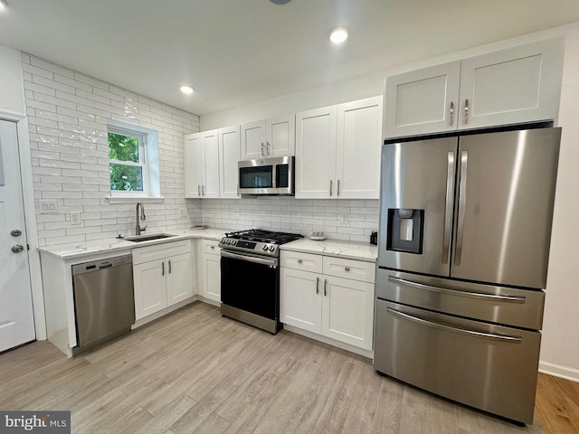 kitchen featuring white cabinetry, sink, light stone countertops, stainless steel appliances, and backsplash