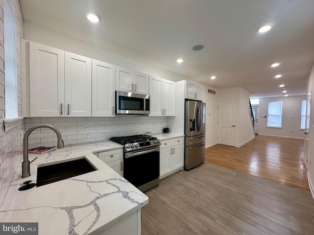 kitchen featuring stainless steel appliances, light stone counters, white cabinetry, and sink