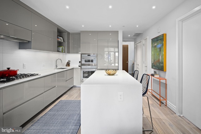 kitchen featuring sink, light hardwood / wood-style floors, gray cabinets, a kitchen island, and appliances with stainless steel finishes