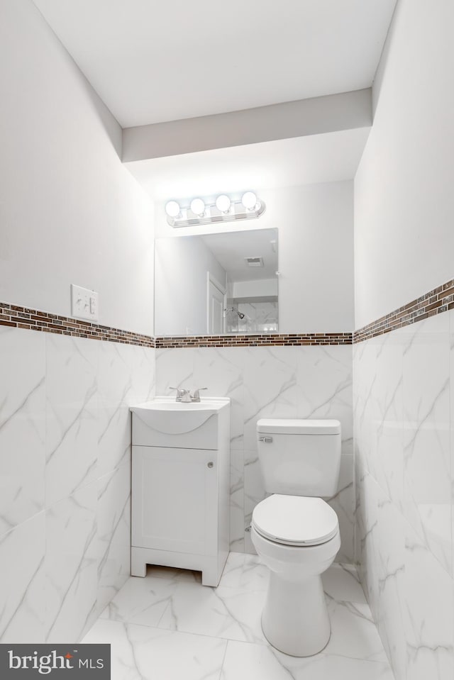 bathroom featuring vanity, toilet, and tile walls