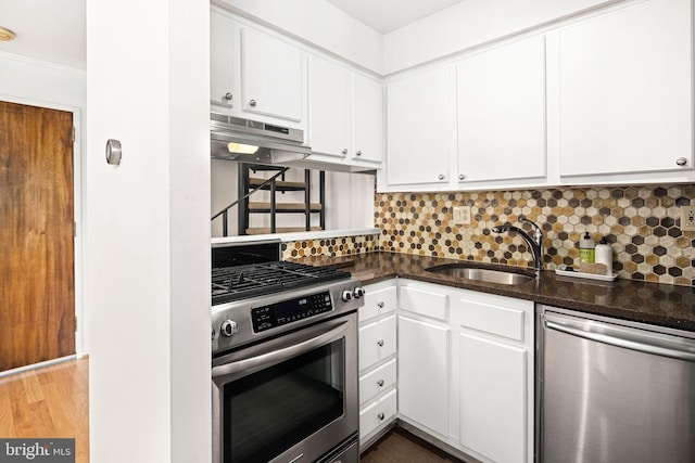 kitchen featuring sink, range hood, dark stone counters, white cabinets, and appliances with stainless steel finishes