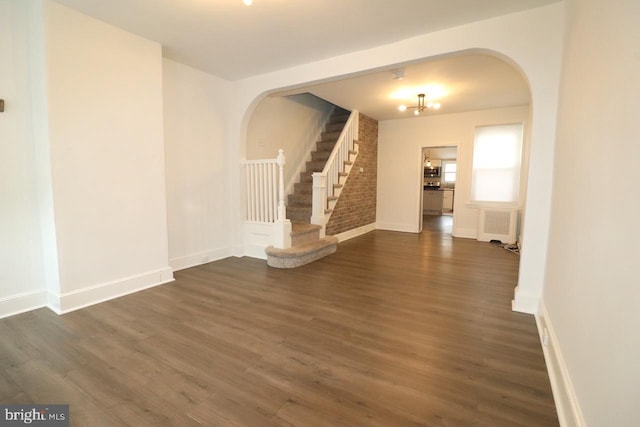 interior space featuring radiator heating unit, dark wood-type flooring, brick wall, and an inviting chandelier