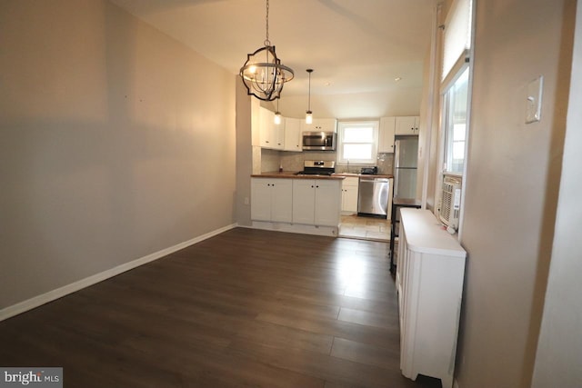 kitchen with decorative backsplash, stainless steel appliances, a notable chandelier, white cabinetry, and hanging light fixtures