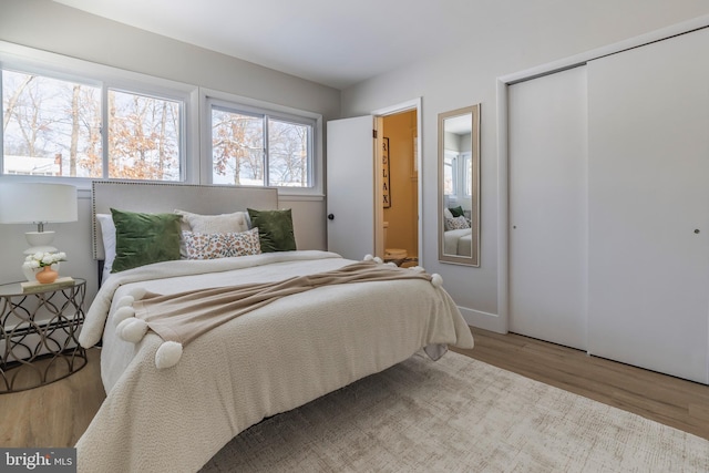 bedroom with light wood-type flooring, a baseboard radiator, ensuite bath, and a closet