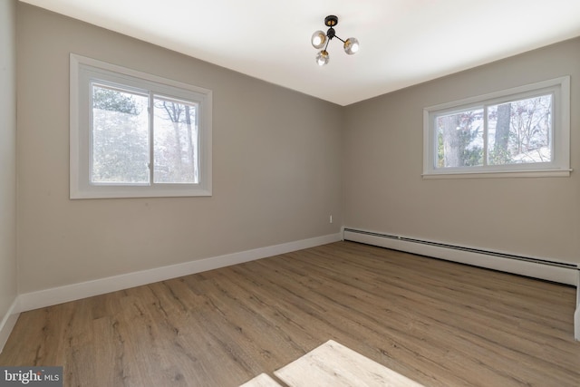 empty room with baseboard heating, a wealth of natural light, light hardwood / wood-style flooring, and a chandelier