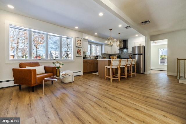 interior space featuring stainless steel refrigerator, a center island, wall chimney range hood, light hardwood / wood-style flooring, and pendant lighting