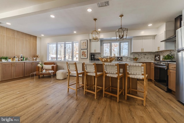 kitchen featuring decorative backsplash, hanging light fixtures, stainless steel stove, and a breakfast bar area