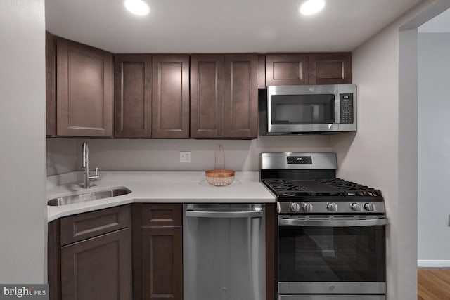 kitchen featuring dark brown cabinetry, sink, light wood-type flooring, and appliances with stainless steel finishes