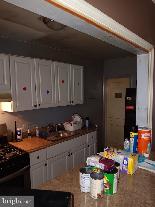 kitchen featuring white cabinets, black gas range, sink, and range hood