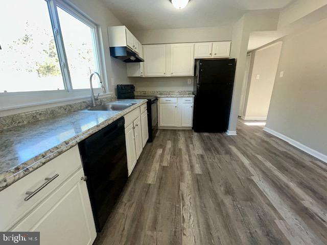 kitchen featuring light stone counters, dark wood-type flooring, sink, black appliances, and white cabinetry