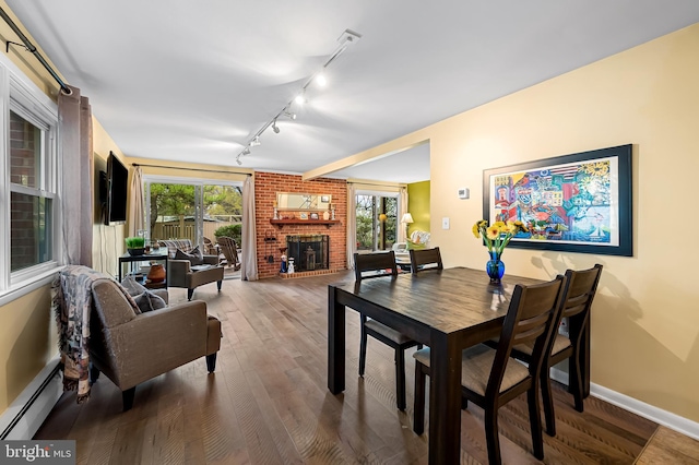 dining space with track lighting, baseboards, a brick fireplace, wood finished floors, and a baseboard heating unit