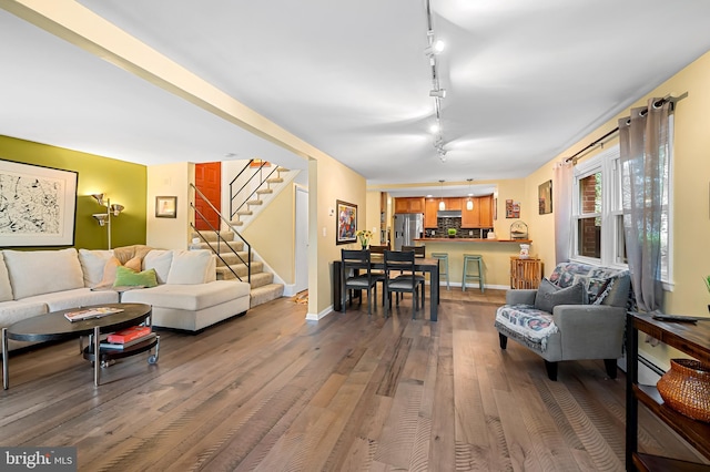 living room featuring track lighting, wood finished floors, baseboards, and stairway