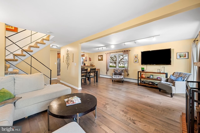 living area featuring rail lighting, wood finished floors, stairs, a baseboard radiator, and baseboards