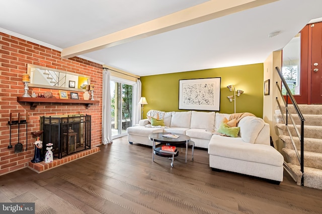 living room featuring wood finished floors, beamed ceiling, a brick fireplace, and stairs