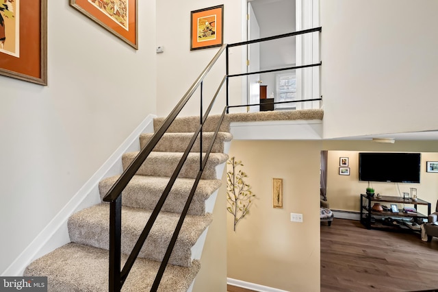staircase with a high ceiling, a baseboard heating unit, wood finished floors, and baseboards
