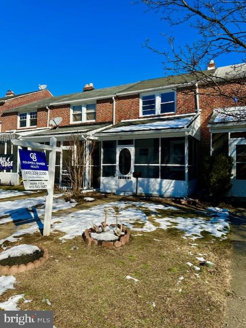 snow covered back of property featuring a sunroom