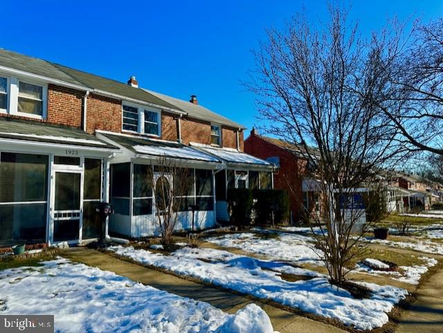 snow covered rear of property featuring a sunroom