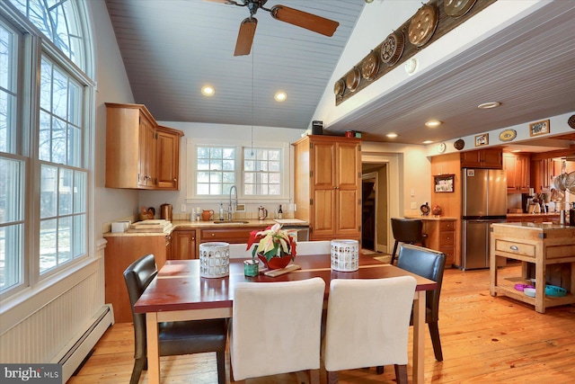 dining space featuring light hardwood / wood-style floors, vaulted ceiling, baseboard heating, and sink