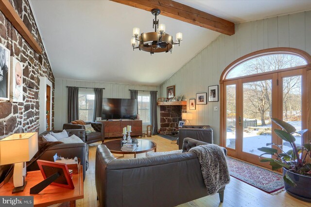 living room featuring vaulted ceiling with beams, a stone fireplace, light wood-type flooring, and a notable chandelier