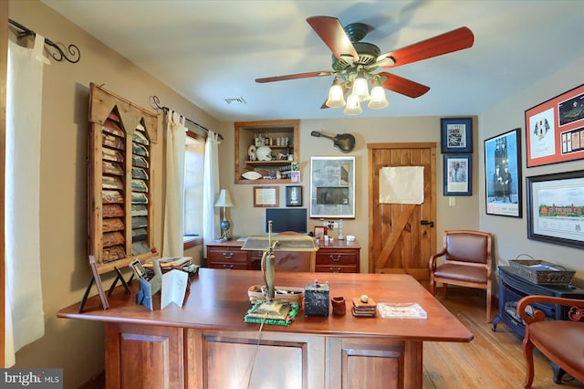 home office with a barn door, ceiling fan, and light hardwood / wood-style flooring