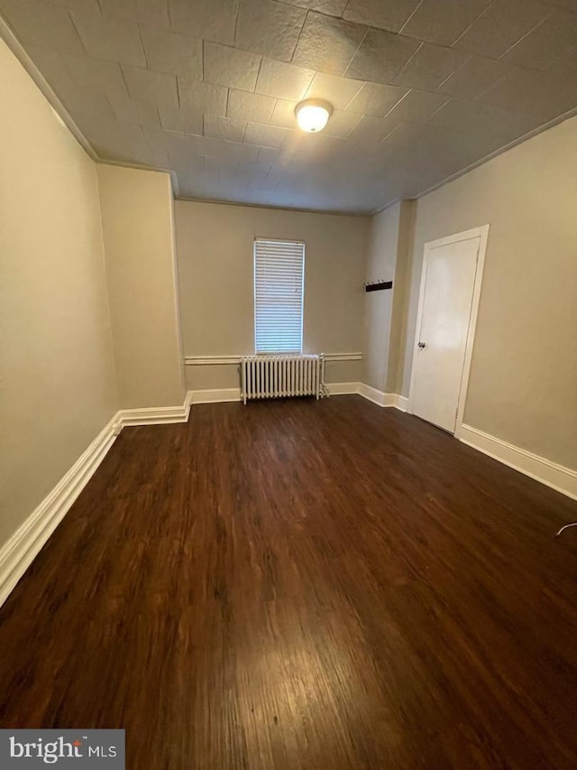 empty room with dark hardwood / wood-style flooring and radiator heating unit