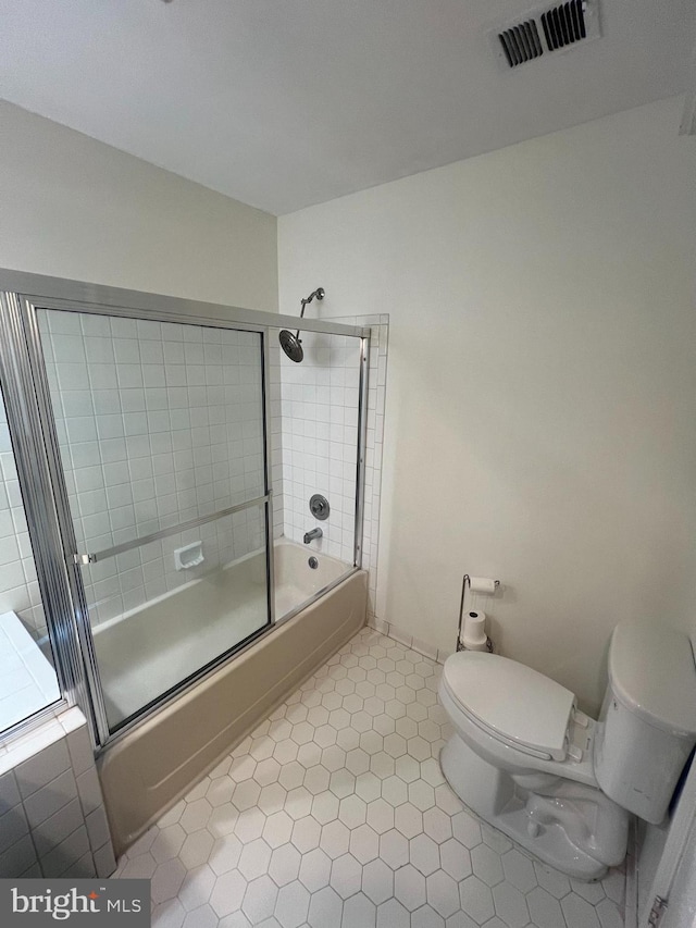 bathroom featuring tile patterned floors, toilet, and bath / shower combo with glass door