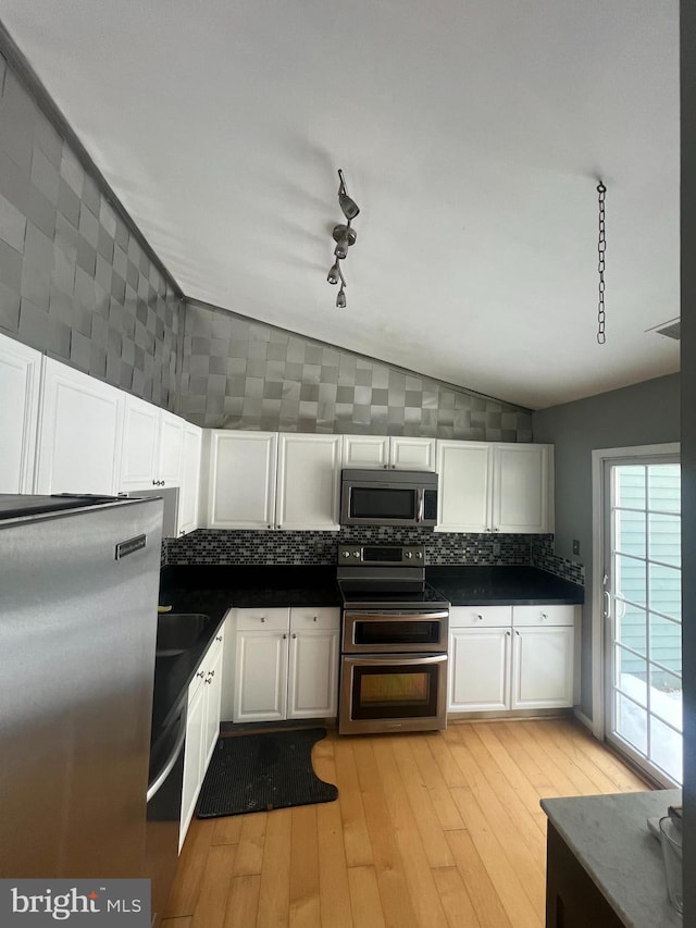 kitchen featuring vaulted ceiling, light hardwood / wood-style flooring, appliances with stainless steel finishes, tasteful backsplash, and white cabinetry