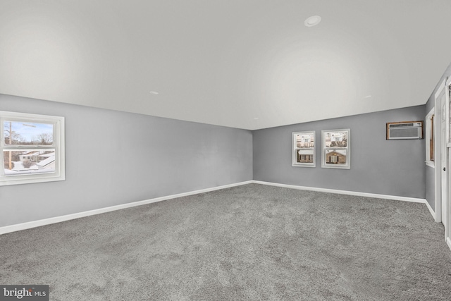 carpeted spare room featuring a wall unit AC and vaulted ceiling