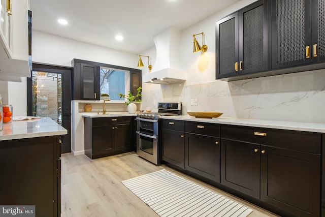 kitchen with custom exhaust hood, range with two ovens, sink, light hardwood / wood-style flooring, and tasteful backsplash