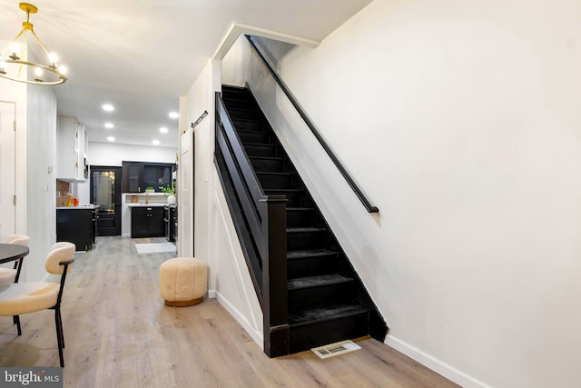 stairs featuring a chandelier, hardwood / wood-style floors, and a barn door