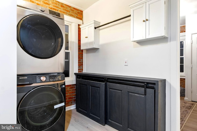 laundry room with cabinets, stacked washing maching and dryer, light hardwood / wood-style floors, and brick wall