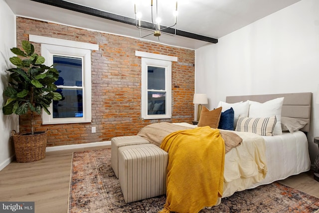 bedroom with light hardwood / wood-style flooring, beamed ceiling, brick wall, and an inviting chandelier