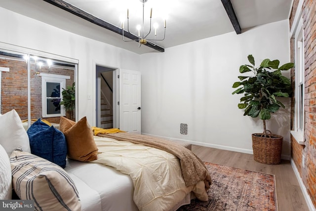 bedroom featuring beam ceiling, wood-type flooring, brick wall, and a notable chandelier